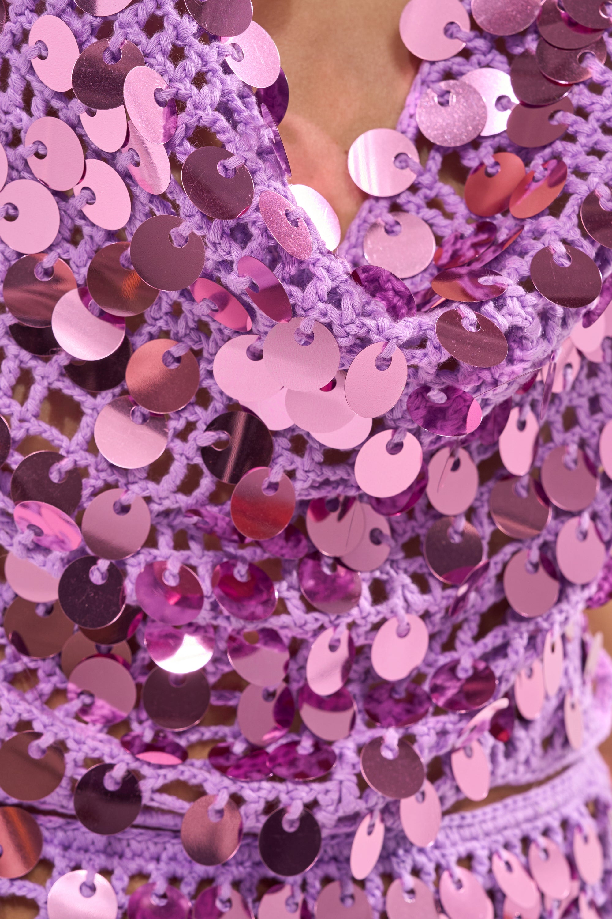 Close-up of the GLOWING CROCHET BRALETTE, a purple halter top featuring large, shiny pink sequins in overlapping rows for a textured, eye-catching look—ideal for standout festival style. 7