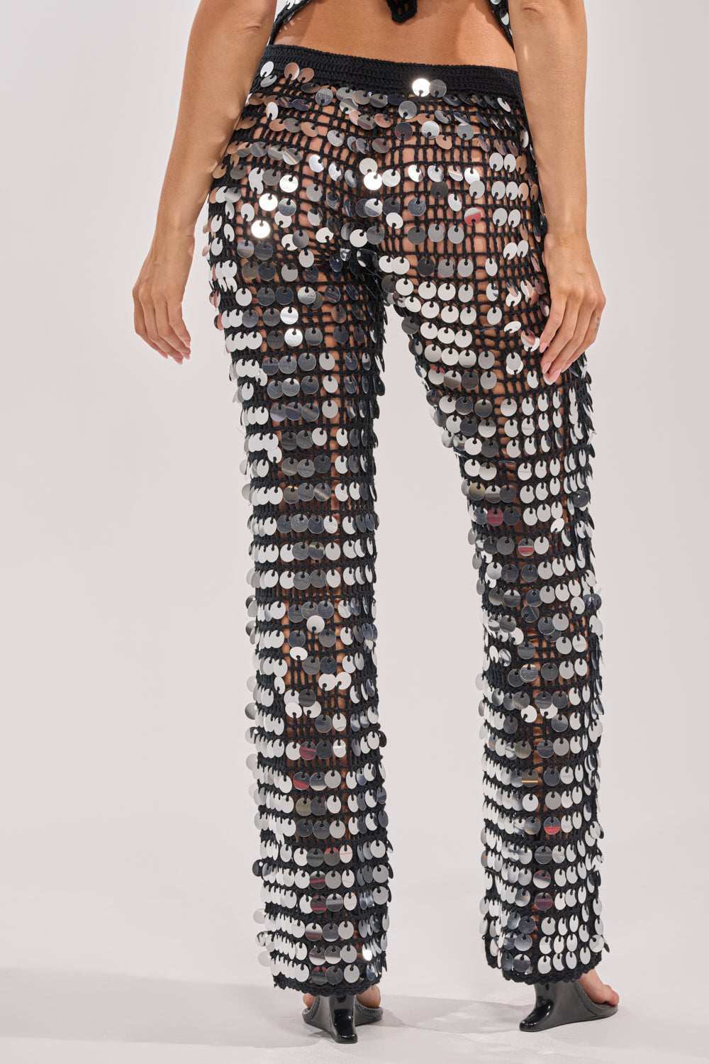 A person stands against a plain background, viewed from the back, wearing the GIVE IT TO ME BABY CROCHET PANT adorned with large, shiny silver sequins. 3