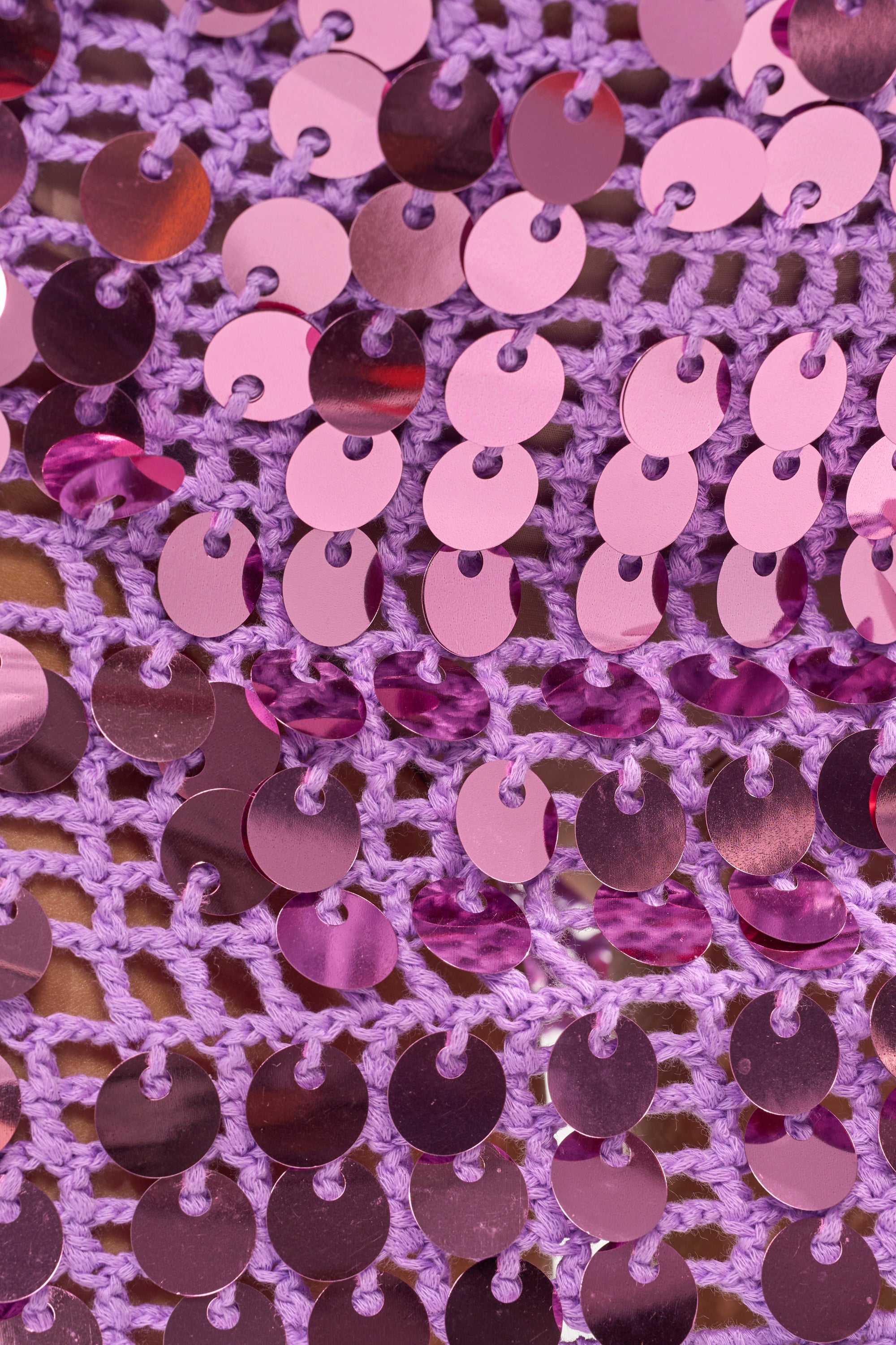 Close-up of shiny, round pink sequins on lavender crochet fabric creates a textured, reflective surface—perfect for party looks or as a detail on the GLOWING CROCHET MINI SKIRT. 8