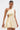 A woman wears the MAKE IT WORK PLEATED MINI DRESS IN YELLOW, featuring an asymmetrical one-shoulder design, pleats, side cutout, and drawstring detail. She accessorizes with a gold clutch and statement earrings, hair pulled back for a chic touch.