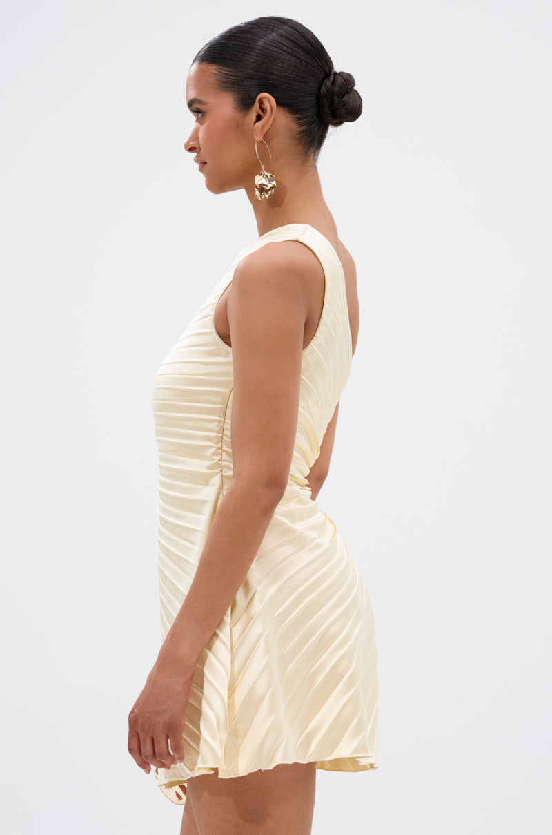 Woman in profile wearing the MAKE IT WORK Pleated Mini Dress in yellow, featuring an asymmetrical one-shoulder design and pleats. She accessorizes with large gold earrings and has her hair in a sleek, low bun against a plain background.