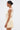 Woman in profile wearing the MAKE IT WORK Pleated Mini Dress in yellow, featuring an asymmetrical one-shoulder design and pleats. She accessorizes with large gold earrings and has her hair in a sleek, low bun against a plain background.