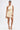 A woman poses against a white background in the MAKE IT WORK PLEATED MINI DRESS IN YELLOW, an asymmetrical one-shoulder mini with pleats and a side cut-out, styled with gold heels, gold earrings, and a matching pleated clutch.