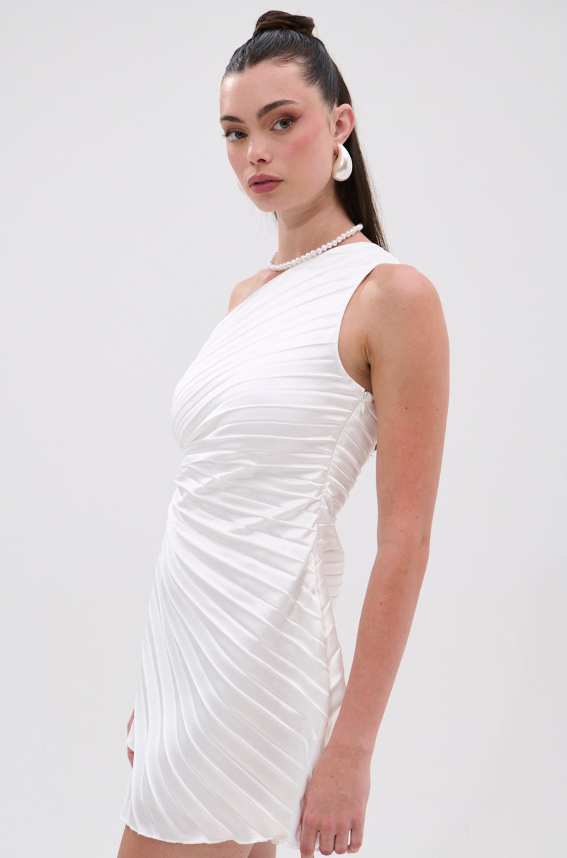 A woman with long dark hair in a high ponytail wears the MAKE IT WORK PLEATED MINI DRESS IN WHITE and large white earrings, standing against a plain light background. 3