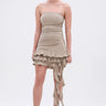 A woman models the COME MY WAY RUFFLE MINI DRESS, featuring a strapless, body-hugging fit with taupe ruching, a ruffled hem, and cascading fabric detail. She pairs it with open-toe heels and hoop earrings against a white background.