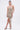 A woman wears the COME MY WAY RUFFLE MINI DRESS—a strapless, body-hugging beige mini with an asymmetrical ruffled hem and long flowing ruffle—paired with heels against a plain white background.