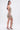 A woman with long dark hair wears the COME MY WAY RUFFLE MINI DRESS, a form-fitting, strapless mini dress with ruffled layers. She stands in profile on high-heeled sandals against a plain white background.