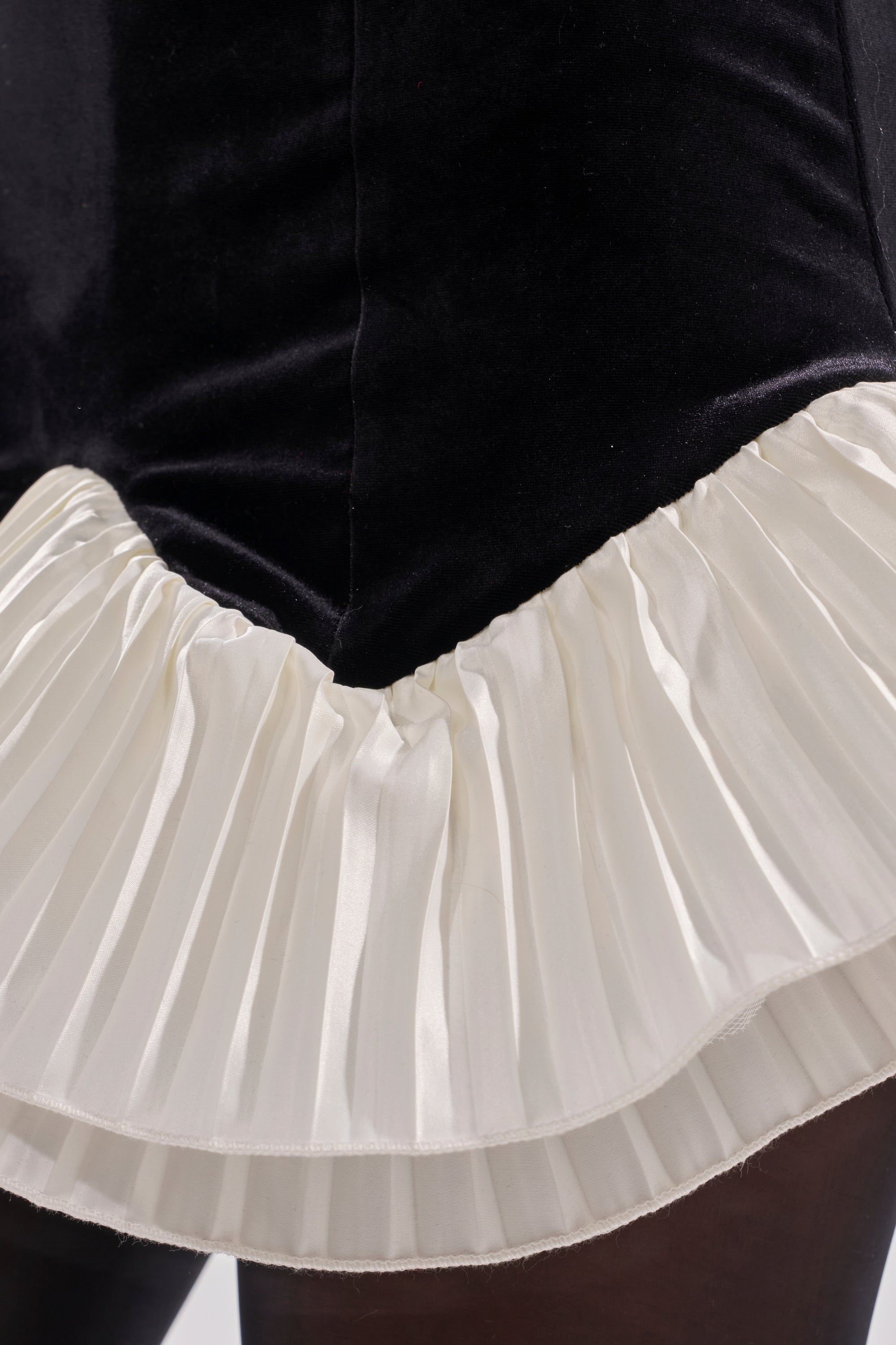 Close-up of the lower part of the BLACK SWAN VELVET MINI DRESS, featuring black velvet fabric and a white pleated ruffled hemline.