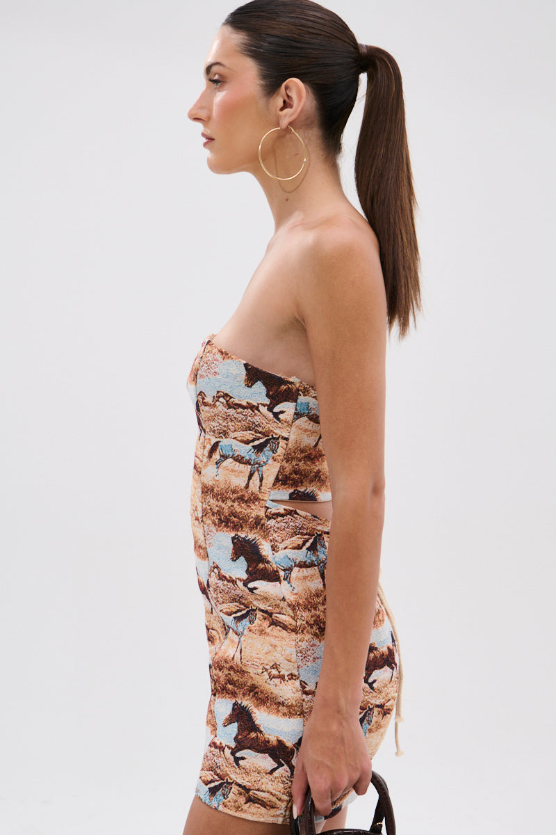 A woman with straight dark hair in a high ponytail models the AINT NO HOLD EM PRINTED MINI DRESS, a strapless bodycon mini with Western horse print. She holds a small handbag and wears large hoop earrings, posing in profile. 4