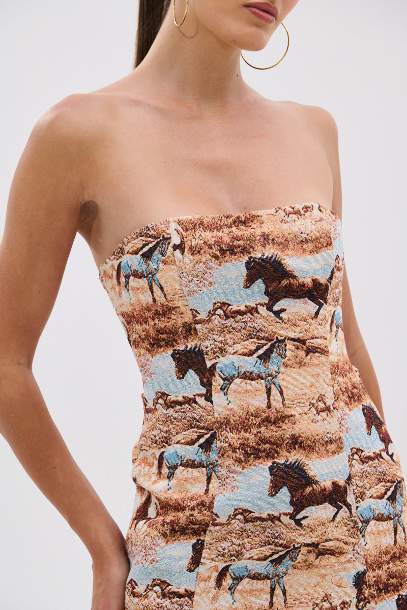 A woman wears the AINT NO HOLD EM PRINTED MINI DRESS, a strapless mini dress with a prairie-inspired Western horse print. She accessorizes with gold hoop earrings and has her hair pulled back; the image is cropped at her mouth and thighs. 8
