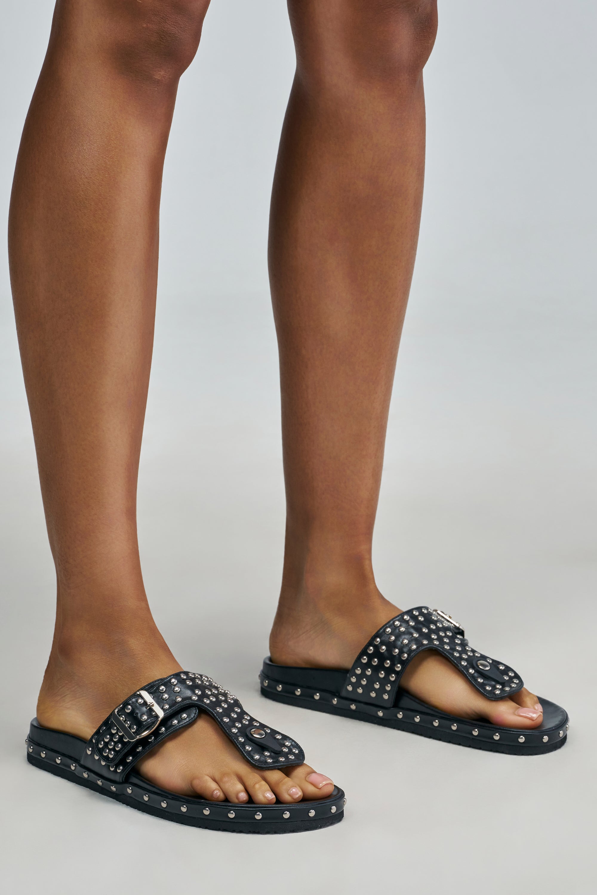 AKIRA GOLD DAISYCHAIN BLACK SILVER EMBELLISHED FLAT SANDAL with silver stud details and a side buckle worn on feet.