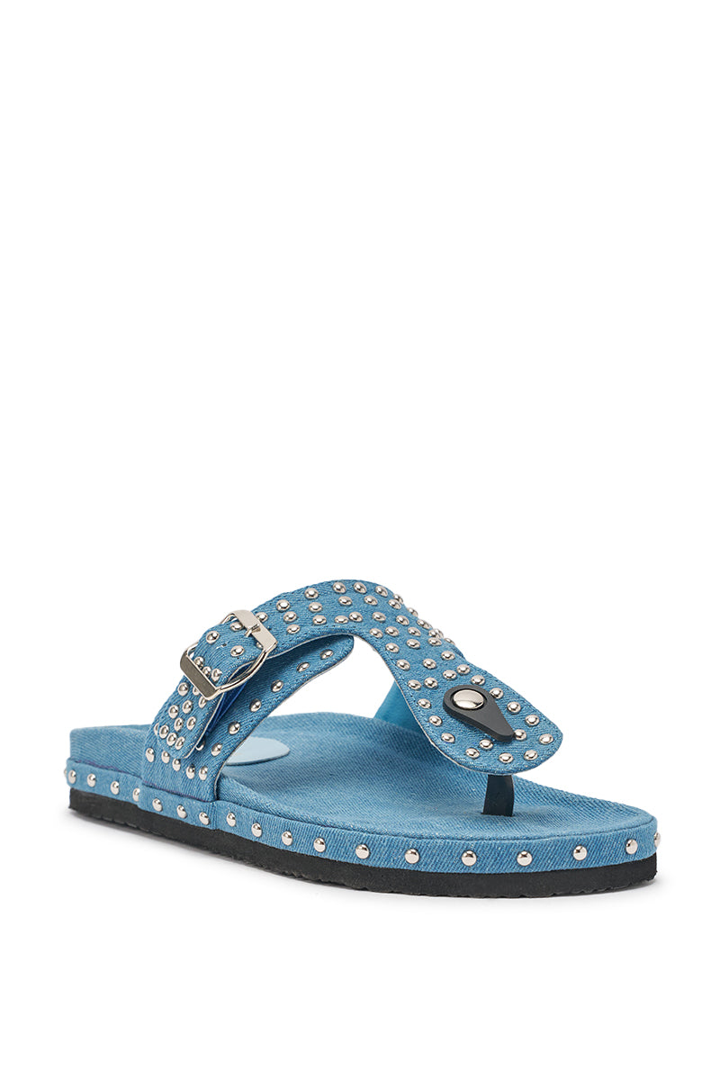 The AZALEA WANG DAISY CHAIN DENIM STUDDED FLAT SANDAL is a blue denim thong sandal with studded details, a buckle strap, flat black sole, and silver accents along the textured edges. 4