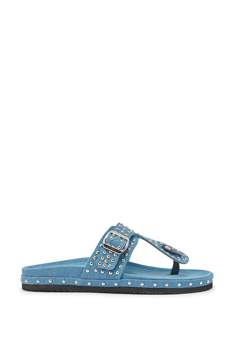 The AZALEA WANG DAISY CHAIN DENIM STUDDED FLAT SANDAL features a blue denim design with a flat sole, silver studs, a large buckle, and studded straps across the toes and diagonally over the foot. 5