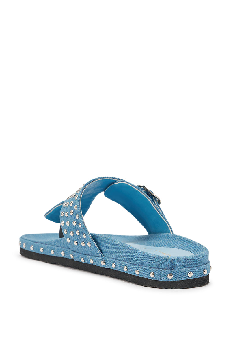 The AZALEA WANG DAISY CHAIN DENIM STUDDED FLAT SANDAL features blue crisscross straps with studded detailing, a black flat sole, and is displayed at an angle on a white background. 6