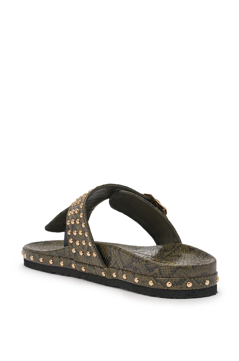 The AZALEA WANG DAISY CHAIN GREEN SNAKE STUDDED FLAT SANDAL features dark green faux snakeskin, crisscross straps with gold studs along the strap and sole edge, shown angled on a white background. 6