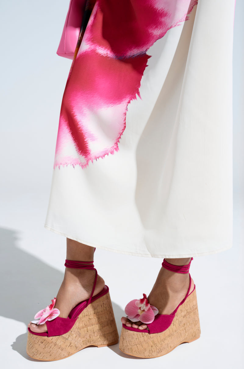 Someone is wearing a white skirt with pink floral patterns and AZALEA WANG DALEYZA FUCHSIA FLORAL WEDGE SANDALS, featuring chunky wedge heels and decorative pink flowers on the toes.