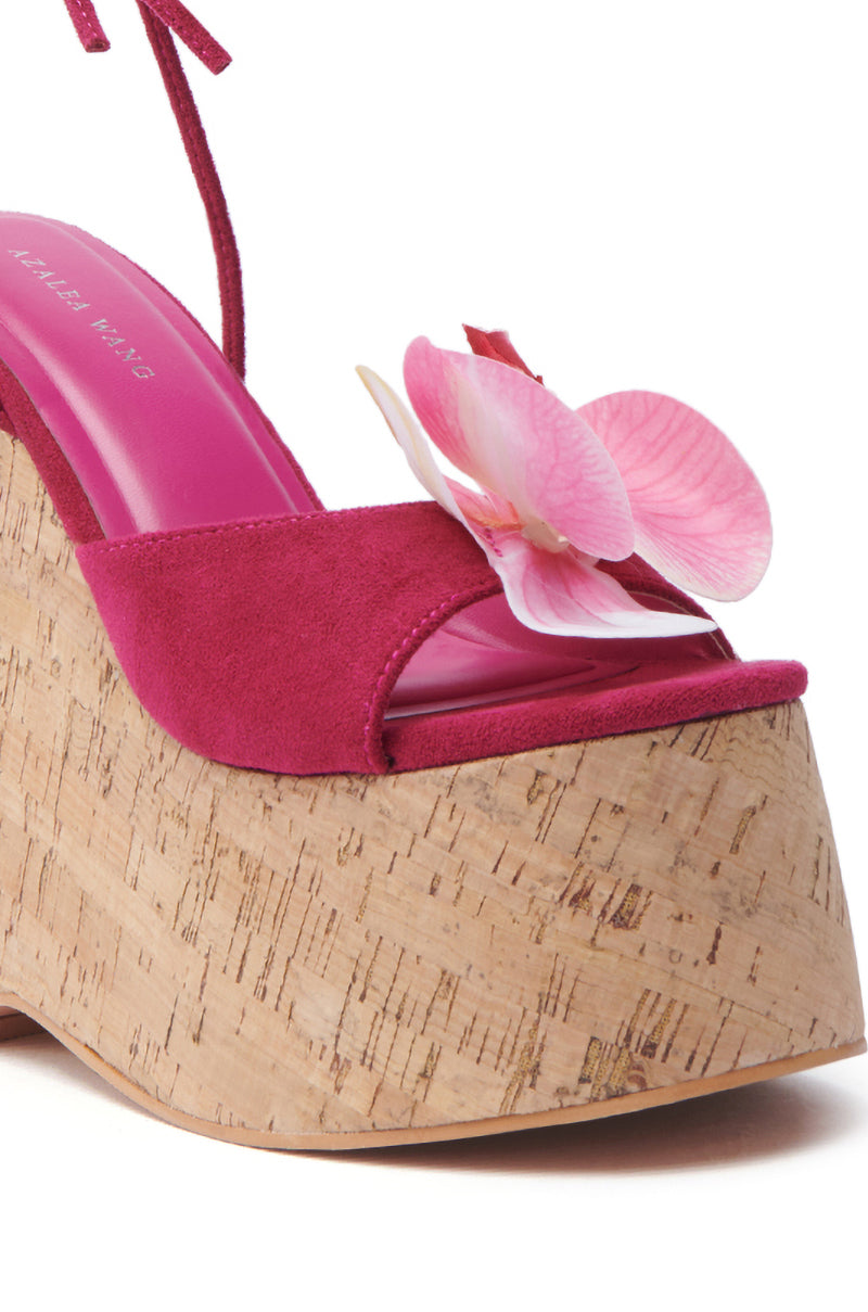 The AZALEA WANG DALEYZA FUCHSIA FLORAL WEDGE SANDAL showcases a fuchsia floral design with a chunky cork wedge heel, open toe, pink suede upper, charming pink flower embellishment, and a color-matching insole.