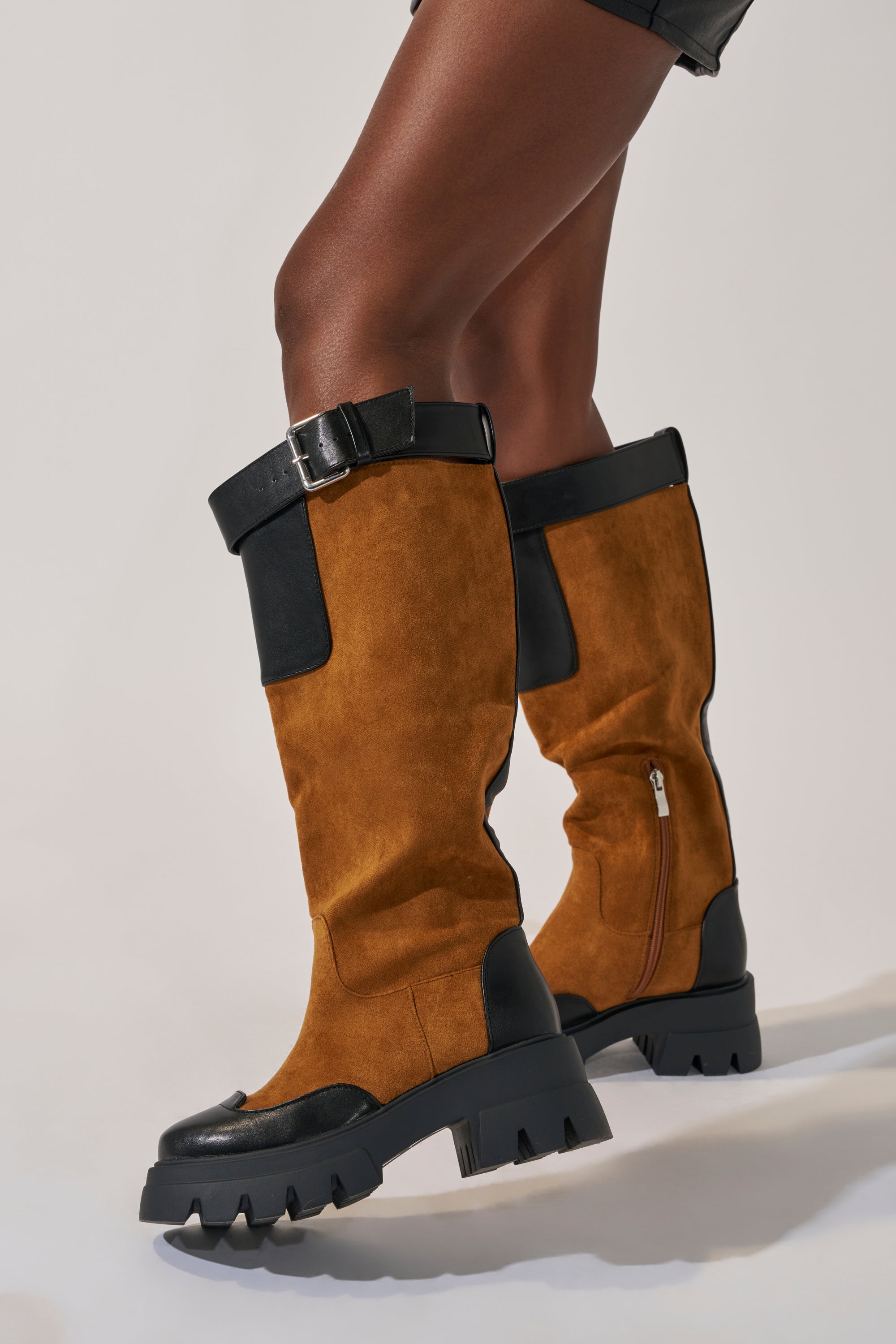 Someone wearing the AZALEA WANG DALILA COLOR BLOCKED FLATFORM BOOT—knee-high, faux suede boots with chunky soles and side zippers—stands against a light background.