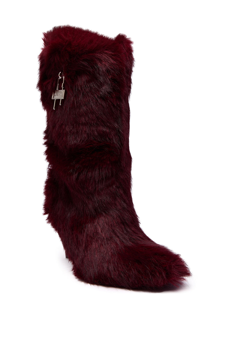 The AZALEA WANG DAMME RED FUR BOOTIE WITH LOCK DETAIL is a tall, pointed-toe bootie featuring dark burgundy faux fur, a hidden wedge heel for subtle height, and a small metallic padlock charm near the top.