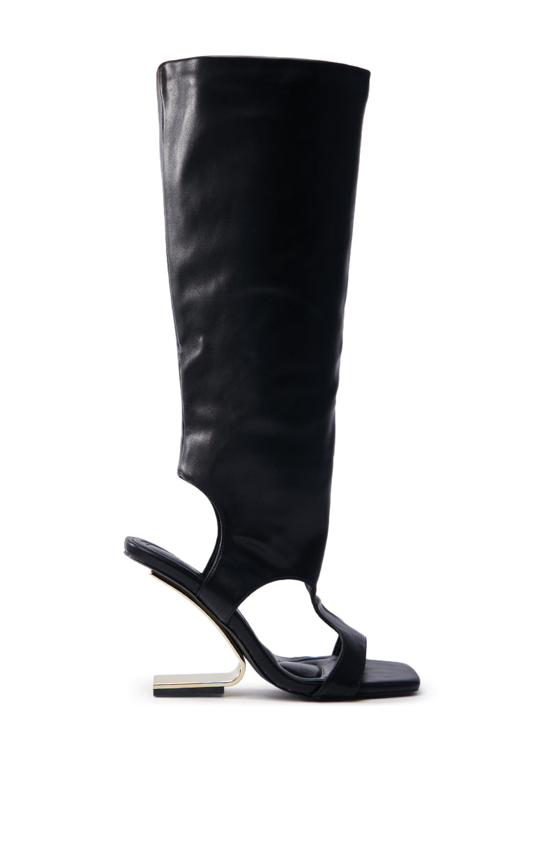 The AZALEA WANG DANALA BLACK GLADIATOR WEDGE SANDAL is a stylish black faux leather boot with an open heel and toe, featuring a unique angular gold heel design. It extends to the knee in sleek lines and includes a comfort cushion insole for all-day wear.