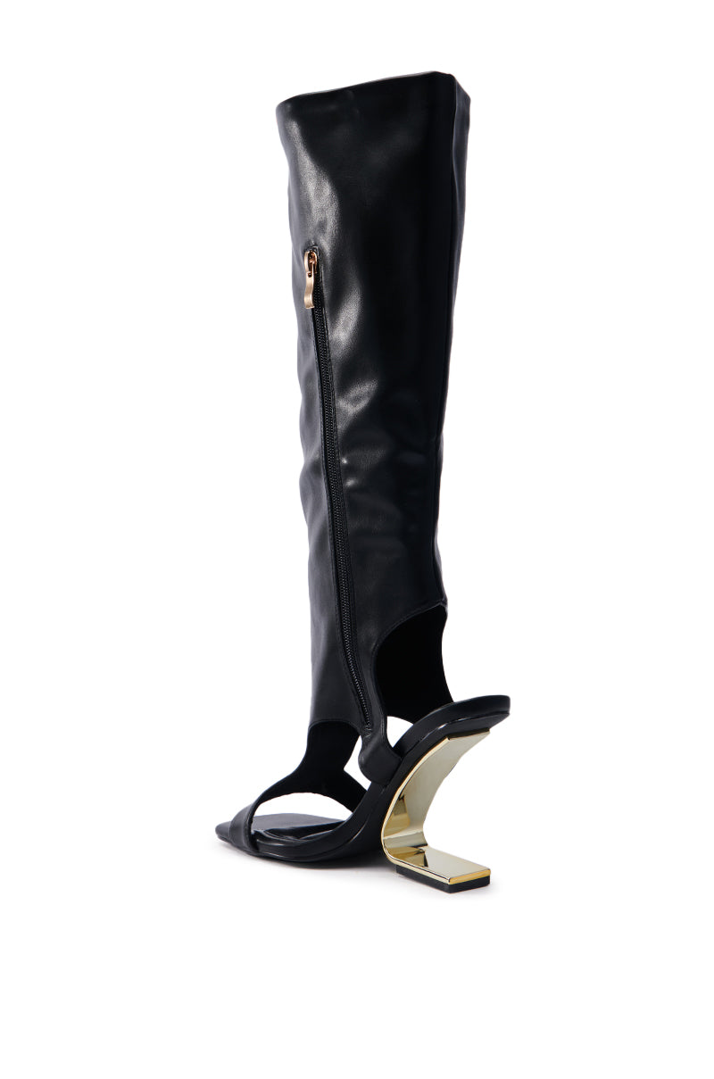 The AZALEA WANG DANALA BLACK GLADIATOR WEDGE SANDAL is a knee-high black faux leather boot with cutouts and a unique gold geometric heel, featuring a comfort cushion insole, side zipper, and a sandal-like front paired with a structured shaft for stylish support.