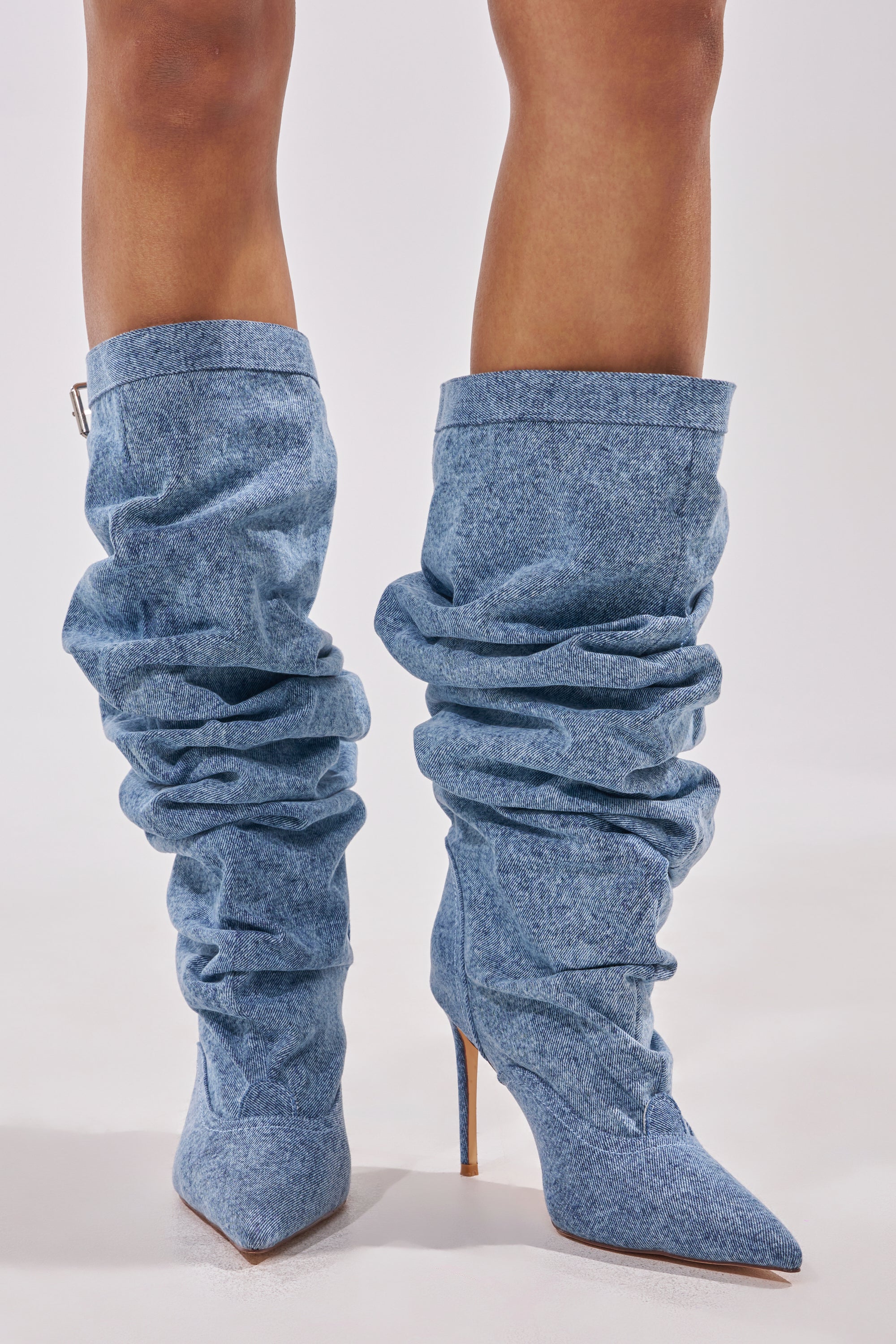 A close-up shows a person wearing the AZALEA WANG DARIA DENIM STILETTO BOOT—slouchy, knee-high denim boots with high pointed stiletto heels—against a plain light background. 2