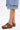 A person in a knee-length denim skirt and AZALEA WANG DARWIN CLOG IN BROWN SNAKE with chunky heels stands against a plain white background.
