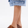 A person in a knee-length denim skirt and AZALEA WANG DARWIN CLOG IN BROWN SNAKE with chunky heels stands against a plain white background.