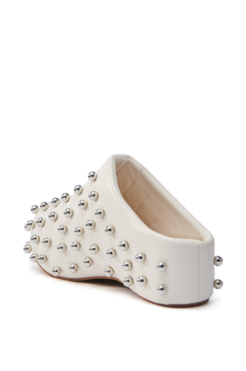 AZALEA WANG DARWIN STUD FLAT CLOG IN BONE: A white faux leather slip-on clog with a low back, decorated with silver metallic studs and featuring a light brown flatform sole, seen from behind and slightly to the side.