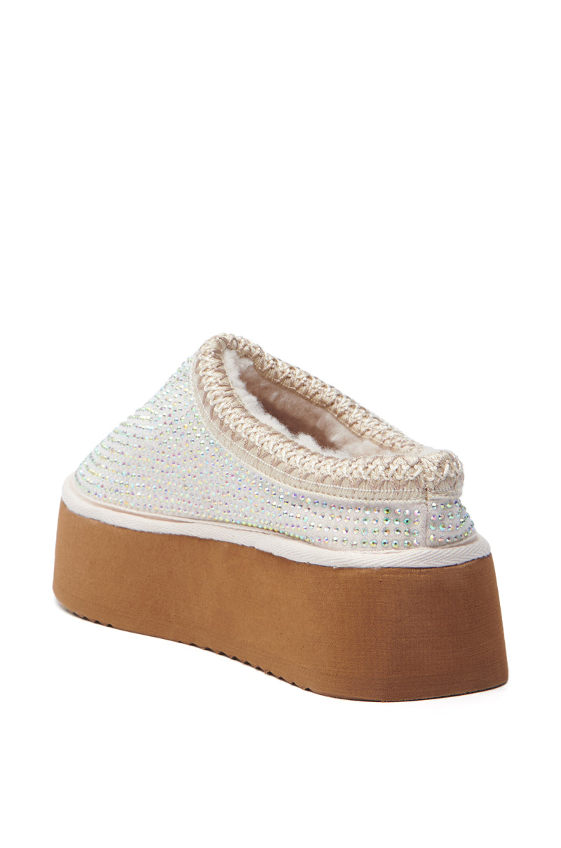 The AZALEA WANG DAVIAT WHITE EMBELLISHED SLIPPER FLAT is a cream-colored slip-on with a shimmering woven upper, subtle rhinestone accents, and a thick brown platform sole. It includes a plush, cozy lining visible around the opening.