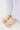 AZALEA WANG DAVIES BEIGE EMBELLISHED FLAT platform clogs, adorned with pearls, beads, jeweled charms, and a plush bunny charm, styled with loose white pants on a light-colored floor.