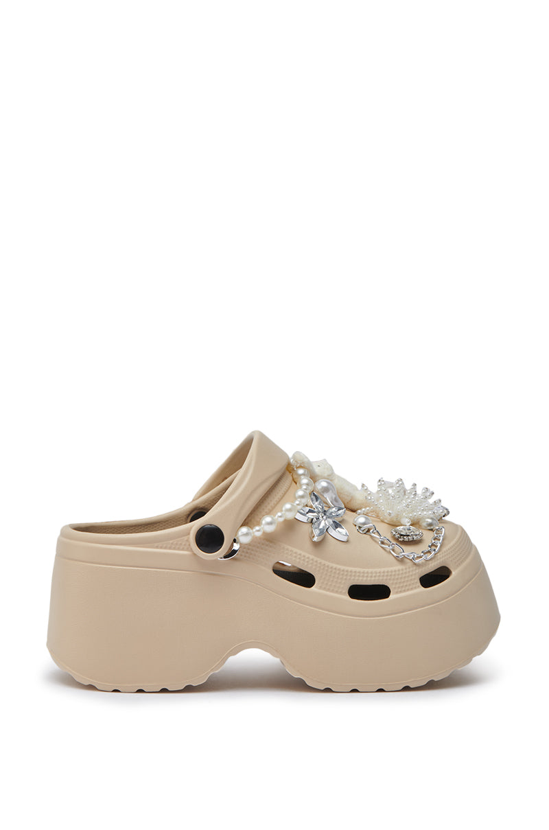The AZALEA WANG DAVIES BEIGE EMBELLISHED FLAT, a platform clog adorned with rhinestones, faux pearls, and crystal-like ornaments, is shown in a side profile against a white background.