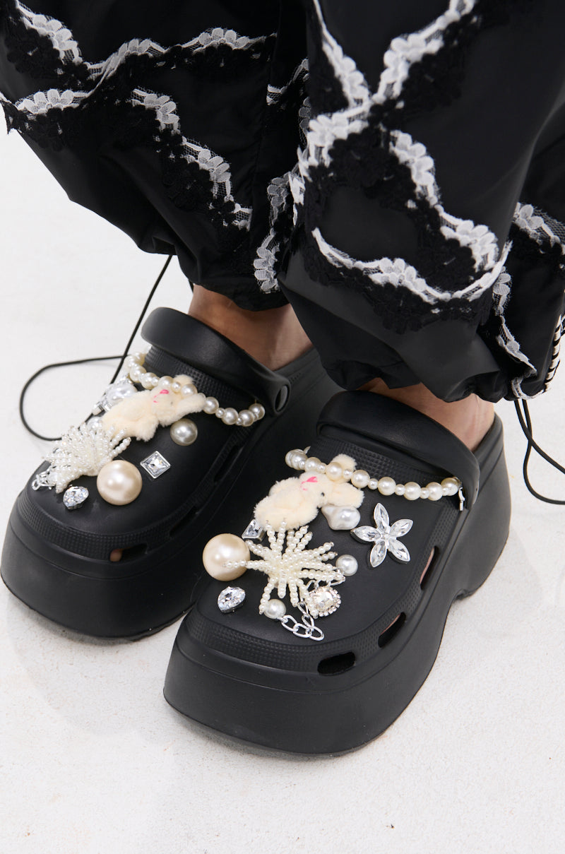 Wearing AZALEA WANG DAVIES BLACK PEARL RHINESTONE FLAT adorned with pearls, beads, faux diamonds, and plush bunny charms, paired with black pants featuring white wavy embroidered patterns.