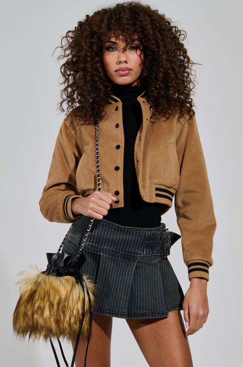 A woman with curly hair wearing the DAVIE EVERYDAY BOMBER and a blue plaid skirt holds a furry teddy knit handbag. She stands against a plain background, posing confidently.