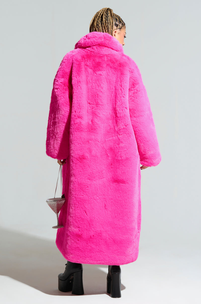 A person with braided hair is wearing the DAYANNE FAUX FUR TRENCH IN FUCHSIA and black platform shoes, holding a small silver handbag. The chic look is set against a plain and neutral background. 5