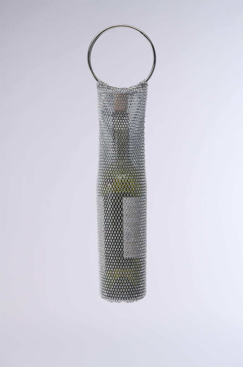 The WINE NIGHTS BOTTLE HOLDER features a wine bottle enveloped in an exquisite metal mesh, elegantly adorned with rhinestone embellishments that form a chic handle. This glamorous accessory stands out beautifully against the plain, neutral background. 1