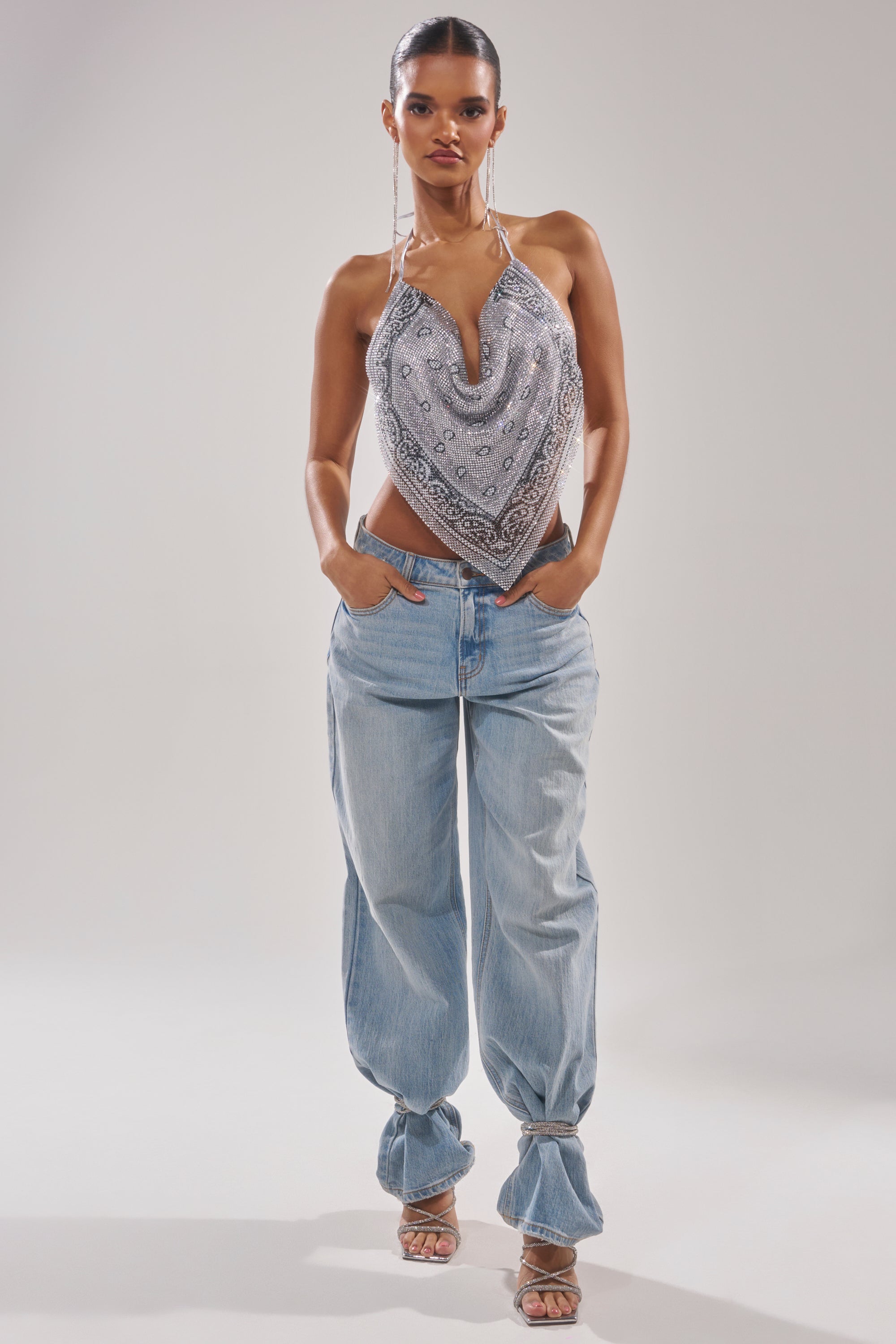 A woman poses in the FREESTYLE RHINESTONE COWL NECK TOP and baggy light blue jeans with tied hems, hands in her pockets, wearing high-heeled sandals against a plain background. 5