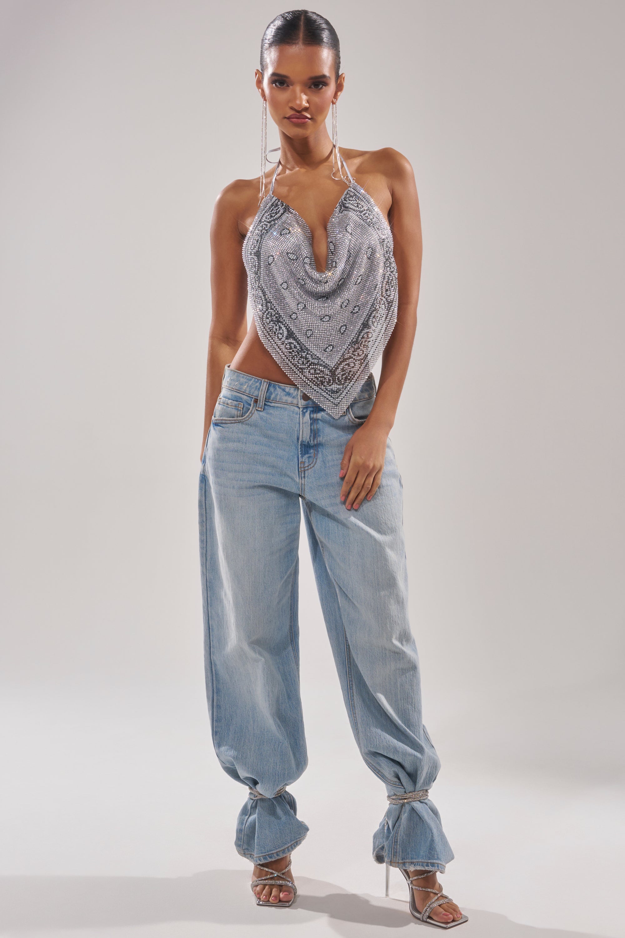A woman poses confidently in the FREESTYLE RHINESTONE COWL NECK TOP, paired with loose light blue cuffed jeans and strappy high-heeled sandals against a plain background. 7