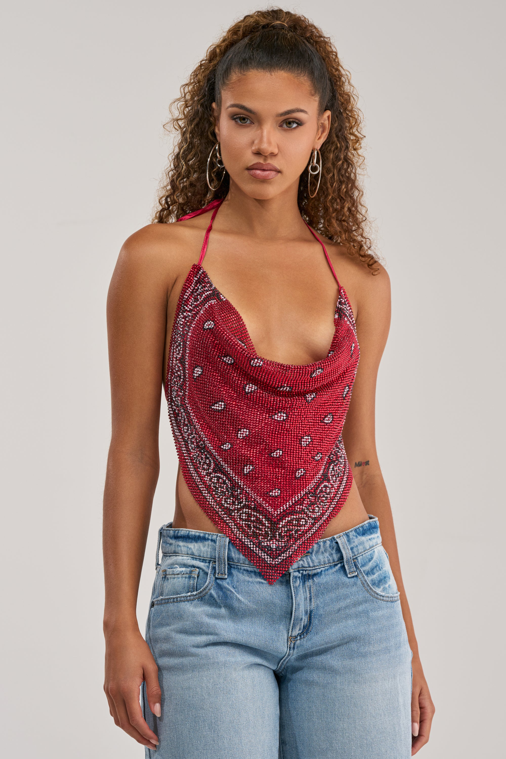A woman with curly hair wears the FOREVER AND EVER COWL NECK BLOUSE and light blue jeans, standing against a plain background—an eye-catching concert outfit.