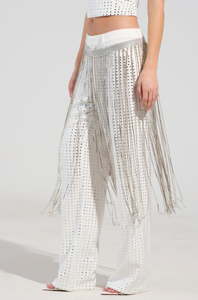 A person wearing the HIS MONEY BLING BELT, featuring white pants with metallic studs and chain link fringe detailing over the legs, matched with a coordinating crop top. The neutral background accentuates the outfit's design and texture.