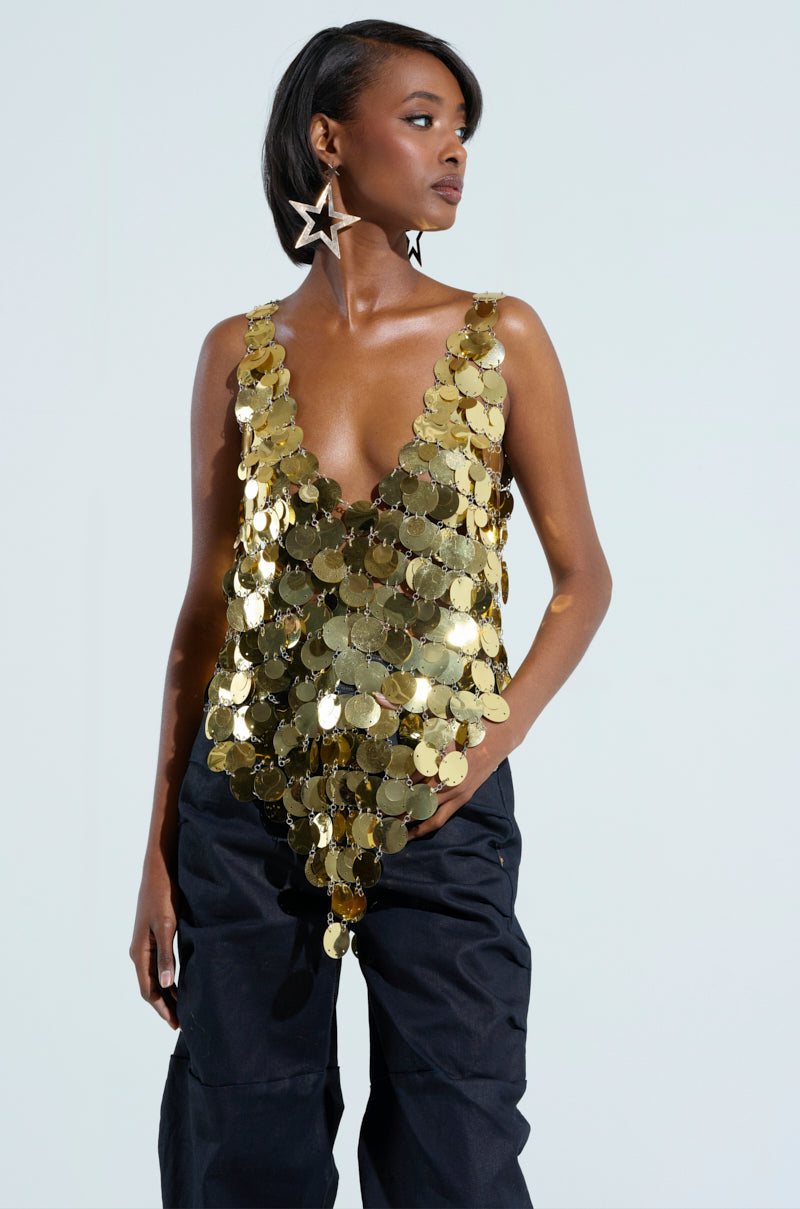 Clad in the GET ME BODIED GOLD SEQUIN TOP featuring a chic V-neckline and complemented by dangling star-shaped earrings, they pair it effortlessly with black pants. Their confident night-out look shines as they pose against a plain background, stylishly gazing to the side.
