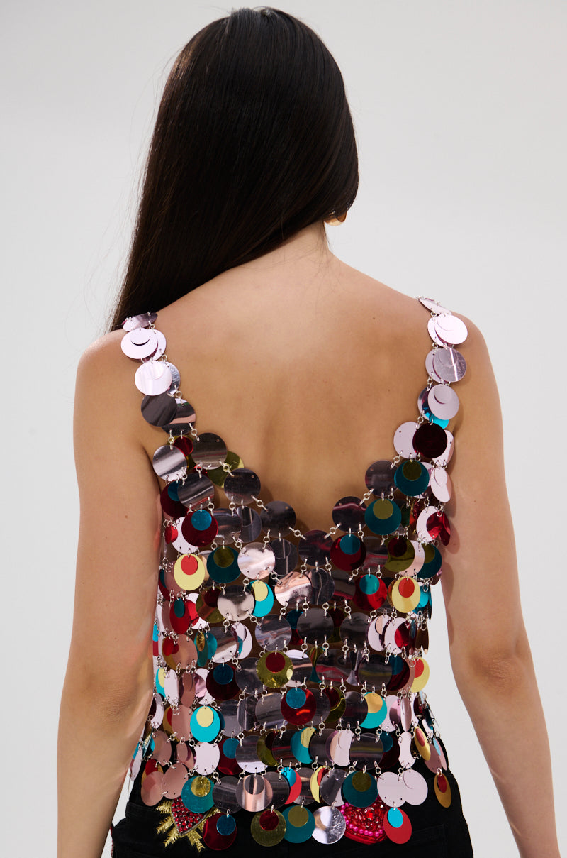 A person with long, dark hair is seen from behind in a DANCING QUEEN EMBELLISHED TOP adorned with bold, multicolored sequins—creating a striking disco look against a simple light background.