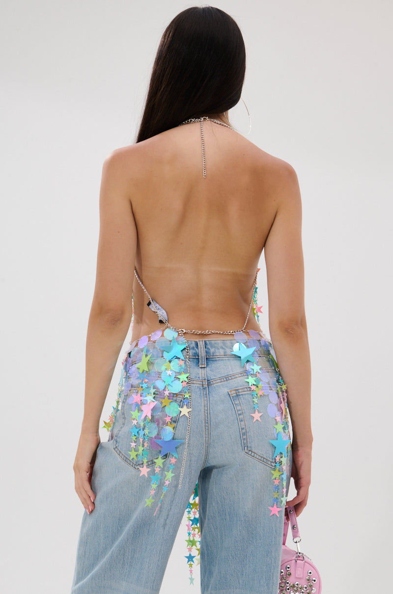A person with long dark hair, seen from behind, wears light blue jeans and the STAR QUEEN BLOUSE with pastel star charms, holding a light pink handbag against a plain white background.