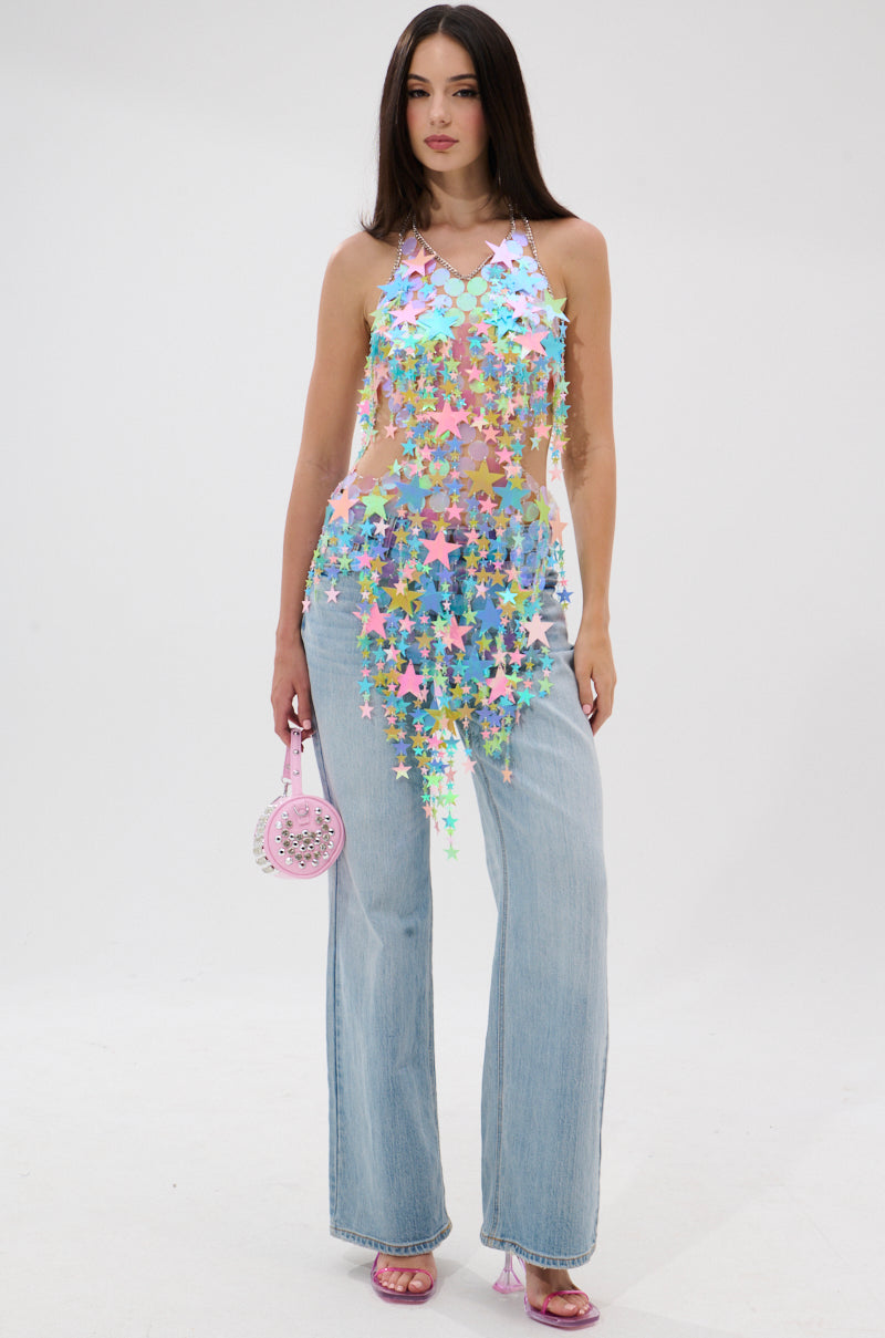 A woman stands against a white background in light blue wide-leg jeans and the STAR QUEEN BLOUSE. She holds a small pink round purse, wears pink heels, and lets her long dark hair fall loosely as she looks forward.