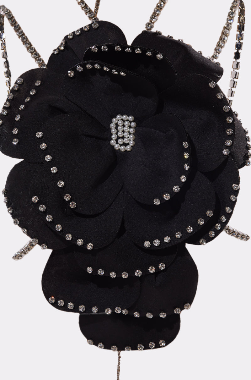 The LET ME BLOOM BODY CHAIN features a black oversized fabric flower embellished with rhinestones along the petal edges and a sparkling rhinestone cluster at the center, displayed on a light background. 8