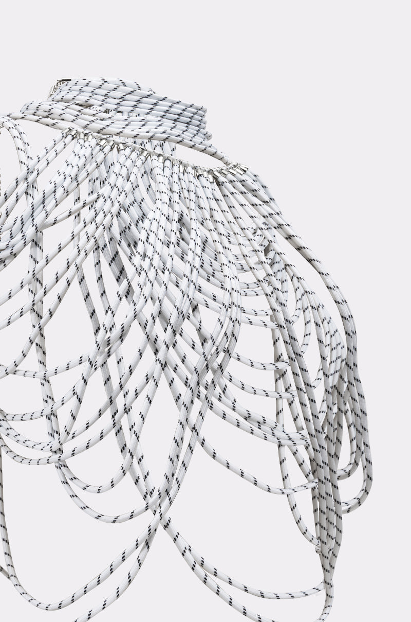The COURTSIDE BODY NECKLACE features layers of white cords with black stripes, artfully draped to create a bold, sculptural cage-like form around the shoulders and upper torso, making a striking avant-garde statement. 6