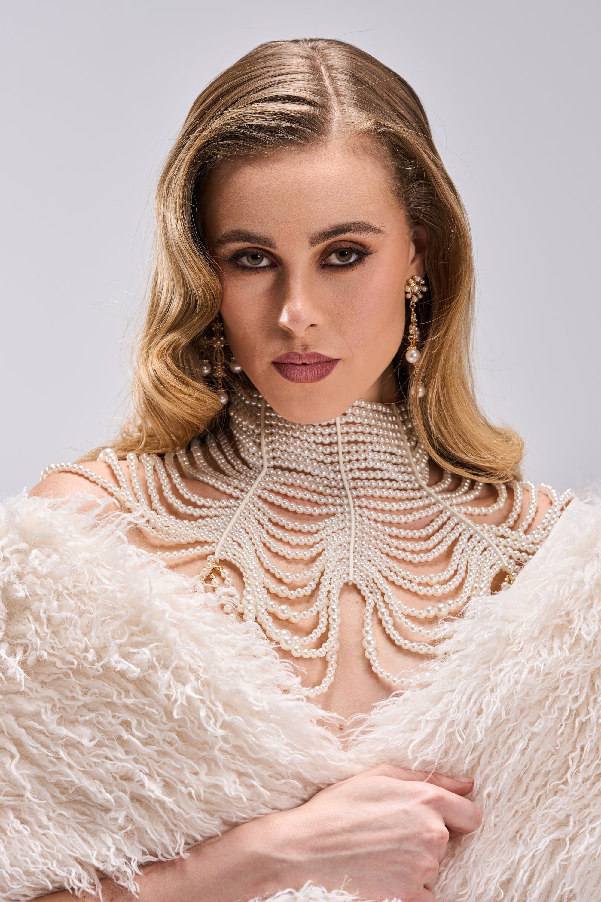 A woman with wavy blonde hair wears the FEELIN DEMURE BODY CHAIN and matching earrings, draped in a textured white shawl, posing against a plain light background and gazing seriously into the camera. 1