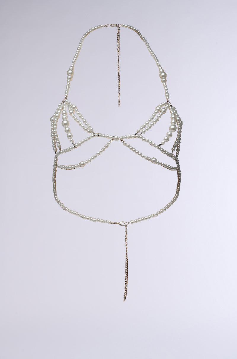 The GIVING CLASS BODY CHAIN is elegantly showcased against a simple white background. The sophisticated design incorporates multiple strands of faux pearl beading and metal chains, creating an adjustable halter neck that wraps around the torso with a long, dangling chain in the center. 1