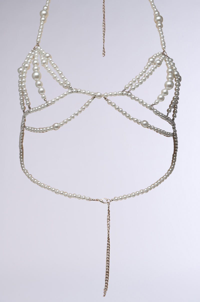 The GIVING CLASS BODY CHAIN is a stunning pearl and metallic silver harness bra adornment that showcases intricate patterns of faux pearl beading connected by delicate gold chains. Its straps and design form an ornate, decorative piece perfect for layering over clothing or wearing as a stylish accessory. 3