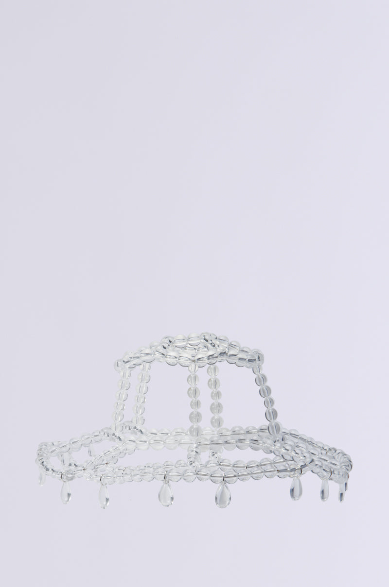 The "CLEAR TO ME DRIPPY BUCKET HAT" is crafted as a transparent glass sculpture, featuring an abstract design with a circular form, dome top, and wide brim. Translucent bead accents dangle like droplets, lending the piece a delicate and artistic look set against a plain white background. 2